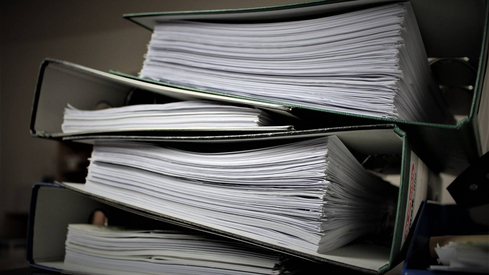 書類がぎっしり綴じられたファイルが積み重なっている様子。社員の資格の書類を会社で整理するイメージ